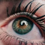 Detailed macro shot of a human eye, showcasing green iris, eyelashes, and reflection.