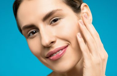 Close-up of a woman smiling with natural makeup on a blue background, showcasing beauty and skincare.